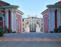 Rundāles pils dzeltenā baroka stila fasāde ar baltiem dekoriem, skulptūrām un centrālo vārtu iebrauktuvi.